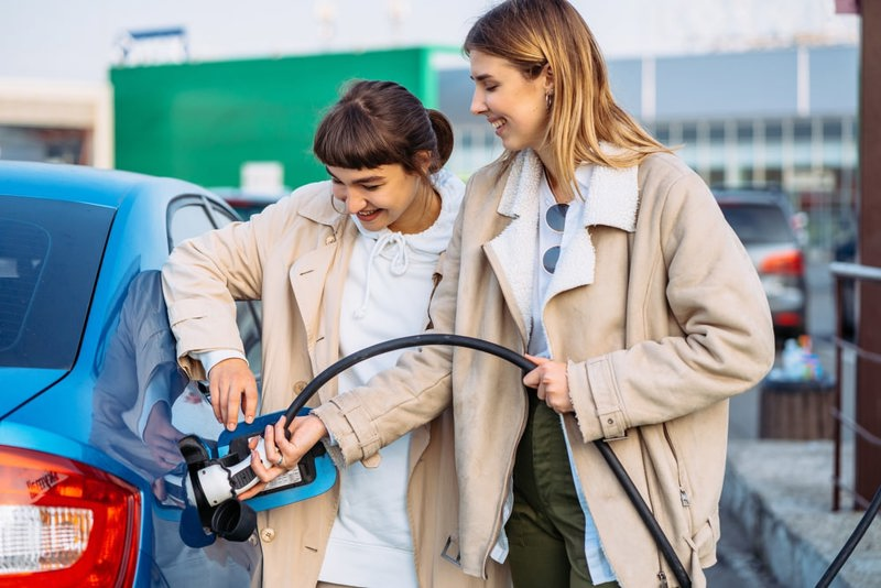 Two young women using smart EV charging for their electric vehicle at a commercial station.